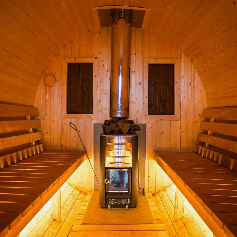 Cozy wooden sauna room with a glowing central wood stove, providing a relaxing atmosphere.